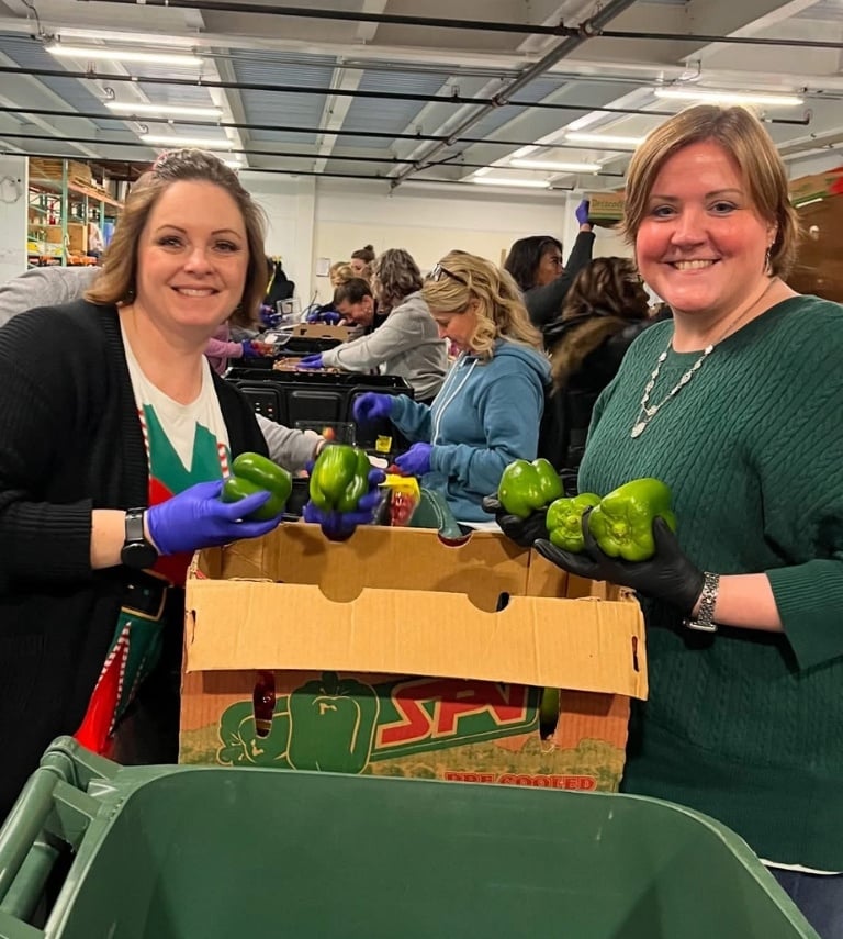 Two woman standing over a box, sorting good green peppers from bad ones. 