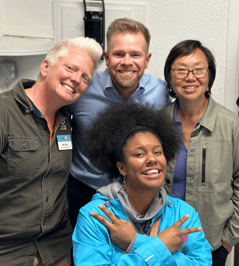 A happy and diverse group of Food Bank of Alaska employees embracing and looking at the camera